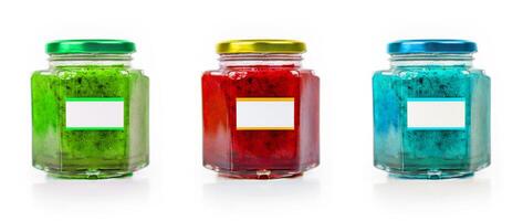 Trio of colorful jam jars with green, red, and blue hues, each with metallic lids and blank label for customizable branding, isolated on white background. Three vibrant marmalade glass jars. photo