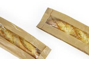 Two freshly baked baguettes, wrapped in brown paper bag, Artisan French baguettes with crispy crusts in paper packaging. Isolated on a white background. Closeup. Copy space photo