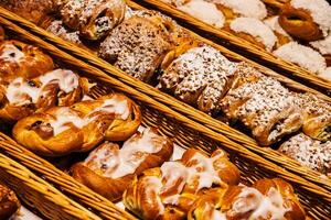 Assortment of freshly baked pastries topped with icing, coconut flakes, and powdered sugar displayed in woven baskets displayed in rustic woven wicker baskets on the shelf of grocery store photo