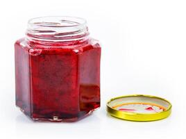 An open hexagonal glass jar of homemade red currant berry or cranberry jam with a gold lid beside it. Freshly made wild berries jelly. Copy space. Isolated on white background. photo
