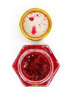 An open hexagonal glass jar of homemade red currant berry or cranberry jam with a gold lid beside it. Freshly made wild berries jelly. Copy space. Isolated on white background. Top view photo