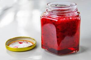 An open hexagonal glass jar of homemade red currant or cranberry jam with a gold lid beside it. Freshly made wild berries jelly. Copy space. photo
