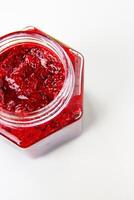 Crop top view of fresh, vibrant red currant berry jam in an open glass jar, perfect for breakfast spreads or desserts. Closeup. Copy space. Isolated on white background. photo