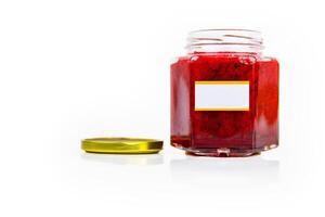 An open hexagonal glass jar of homemade red currant berry or cranberry jam with a gold lid beside it. White blank label for custom text. Copy space. Isolated on white background photo