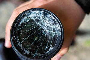 Closeup of a hand holding a broken shattered camera lens with visible cracks, symbolizing damage and fragility of photography equipment, repair or replacement needs, accidents, or fragility. photo
