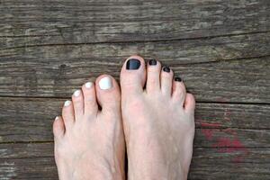 Bare feet with black and white painted toenails resting on the wooden floor. Two feet with contrasting nail polish, symbolizing individuality, personal style and relaxation. Copy space photo