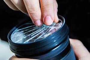 Closeup of a hand holding a broken shattered camera lens with visible cracks, symbolizing damage and fragility of photography equipment, repair or replacement needs, accidents, or fragility. photo