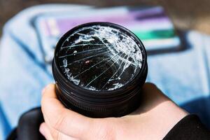 Closeup of a hand holding a broken shattered camera lens with visible cracks, symbolizing damage and fragility of photography equipment, repair or replacement needs, accidents, or fragility. photo
