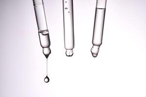 Three pipettes with a cosmetic product. Serum or fluid drips from one of them. photo