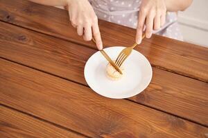 Minimalist dining. hands cutting macaron with fork and knife on wooden table. photo