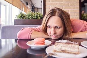 Woman contemplates dessert choices in cafe with focused expression and sweet temptations in background. photo