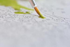 Close-up of a paintbrush adding green to a detailed paint-by-numbers canvas. photo
