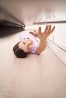 Woman reaching under furniture for lost item in modern home interior, expressing determination and focus. photo