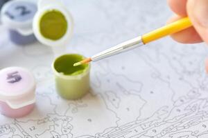 Hand holding brush over paint by number kit for relaxing art activity at home. photo