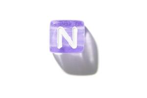 Purple translucent block with letter n casting shadow on white background. photo