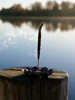A small incense stick sitting on a wooden post near a lake photo
