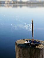 A small incense stick sitting on a wooden post near a lake photo
