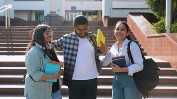 Three Indian students posing in front of college, looking at camera and hugs video