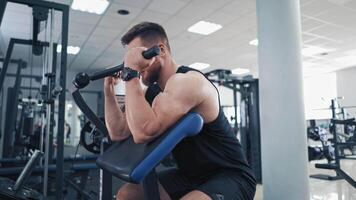 Bearded man pumping his arm muscles in the gym. Athletic bodybuilder training his biceps on a modern simulator and looking confidently forward. video