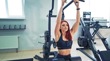 Fitness coach of the sports club does pulls on the simulator for strengthening the shoulder muscles. Attractive sporty woman is engaged on a simulator for the muscles of arms. video