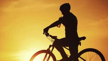 Silhouette of professional bicyclist taking a bottle and drinking water at golden sunset. Male cyclist in helmet drinks water on the natural background of setting the sun in the evening. video