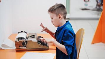 Boy sitting at table and typing old typewriter. video