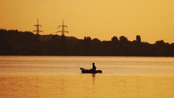 Silhouette of a man floating in a boat on the river surface on the background of an evening trees. Fisherman roams with oars while sailing on a row boat in the lake at beautiful sunset. video