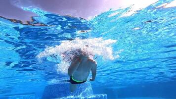 Underwater of a boy swimming in blue clear water. Little boy dives under the water with closed eyes in the swimming pool. video