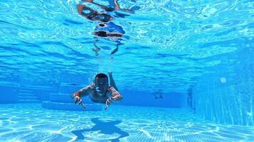 Vacation concept. Happy young man swimming inside the swimming pool. Man is diving under the water and moving forward to camera. video