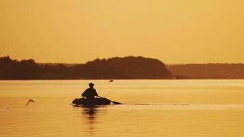 Silhouette of man sailing with two wooden oars on a small boat at sunset time. Beautiful sunset in the river and the silhouette of a man who tries to find a place for fishing on rowboat. video