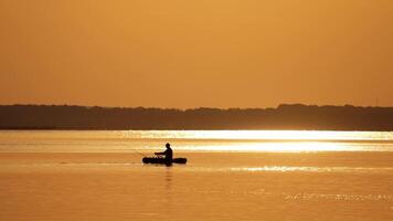 Fisherman in a boat at golden sunset time. Silhouette of man floating with oars on a small rowboat in the evening. Beautiful sunset in the river and man in boat with fishing rods. video