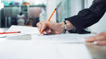 Close-up of seamstress hand with a sharp pencil draws a sketch of a stylish dress on a paper. Woman's hands are making a pattern sketch of a future clothing in atelier. Feminine hobby. video