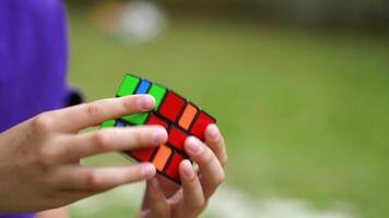 Close-up of rubik's cube in boy's hands. Boy is holding rubik cube and solving puzzle of one of the world's best-selling toys on blur green background. video