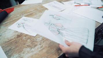 Hands of a tailor putting papers with stylish sketches on the table. Modern creative works of a fashionable designer is sorting by a seamstress in atelier. video