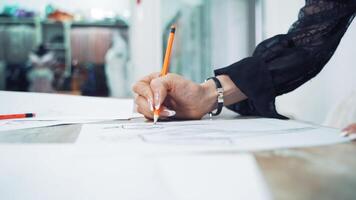 Hands of a professional tailor is drawing a sketch with a sharp pencil on a table. Dressmaker is making a creative design of a dress on a sheet of paper in her workplace. video