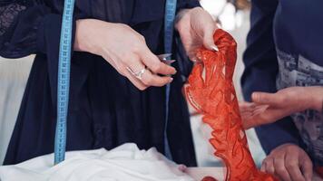 Professional dressmaker is cutting red lace with scissors with the help of a tailor in atelier. Woman's hands cutting out sequin and beaded red lace along its edge following the contour. video
