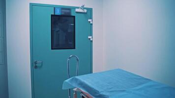Blue door of the operating room and medical cart for carrying injured patients. Empty light corridor and a new gurney in the clinic indoors. Motion camera back. video