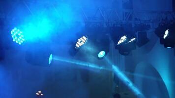 Thick smoke and many projectors hanging on the ceiling on the blue blurred background. Flashing rays from spotlights in the evening indoors. video