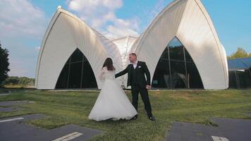 Smiling wedding couple posing in front of modern building, modern white building under a vibrant sky. video