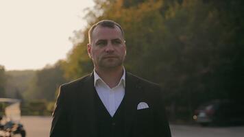 Groom portrait in a peaceful outdoor setting, surrounded by lush greenery and soft evening light, creating a contemplative and classic portrait. video