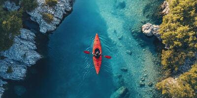 Aerial View of a Single Kayaker Paddling Through a Narrow Channel in a Pristine Lake Surrounded by Lush Green Trees and Rugged Rocky Cliffs photo