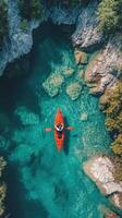 Aerial View of a Single Kayak Paddling in a Turquoise Lake Surrounded by Rocks and Trees photo
