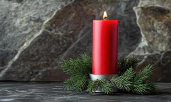 A red candle is lit on a table with pine needles photo