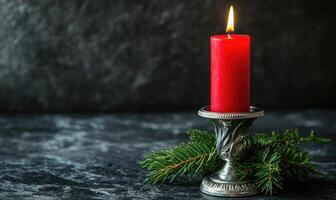 A candle is lit on a table with a pine branch photo