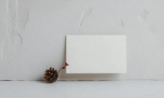 A white card with a red ribbon is on a table next to a pine cone photo