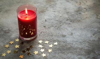 A red candle is lit in a glass container on a grey surface photo