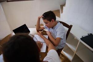 Boys collaborating on homework at a wooden table with tablet photo