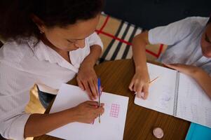 Mother helping child learn math at home on a wooden table photo