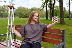 Young female with a casted leg pausing on a bench to take a self-portrait, preserving a moment of her rehabilitation journey and the challenges faced in the tranquil summer setting photo
