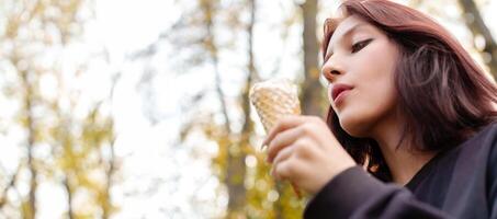 Teenage girl with striking looks playfully savors creamy ice cream cone in autumn park, tongue piercing adding hint of intrigue photo